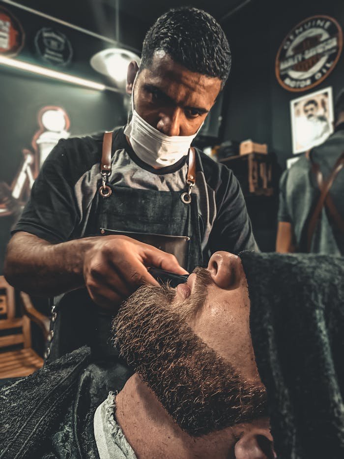 A barber meticulously trims a client's beard in a modern barbershop setting.